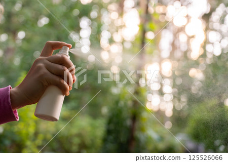 Hand applying insect repellent mosquito insecticide spray to kill flies bugs and mosquitoes on skin outside. Malaria zika virus and dengue fever prevention 125526066