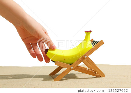 A hand sets a banana on a tiny beach chair, summer vibes, isolated on white background A hand sets a banana on a tiny beach chair, summer vibes, isolated on white background 125527632