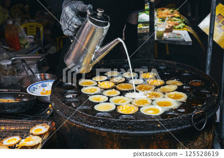 cooking a traditional Vietnamese dish Banh Khot with corn at an Asian night market on street in Vietnam in Asia cooking a traditional Vietnamese dish Banh Khot with corn at an Asian night market on street in Vietnam in Asia 125528619