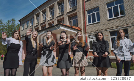 Smiling students making a stop gesture in front of their school on a sunny day Smiling students making a stop gesture in front of their school on a sunny day 125528987