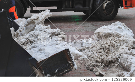 Tractor shovel loading dirty snow into a truck during snow removal in winter 125529009