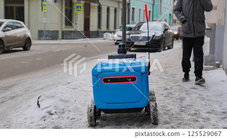 Autonomous delivery robot moving on a snowy sidewalk in Moscow. Autonomous delivery robot moving on a snowy sidewalk in Moscow. 125529067