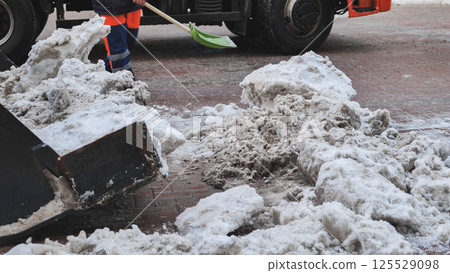 Municipal worker removing snow from street with shovel and truck 125529098