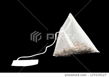 Pyramid shape tea bag isolated on black background with clipping path. Close-up of fresh herbal tea bag isolated over black background 125529127