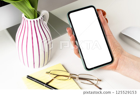 Smartphone mockup in woman hand. New modern black frameless smartphone mock up with blank white screen. Empty space for text. Copy space. Isolated white blank screen. 125529153