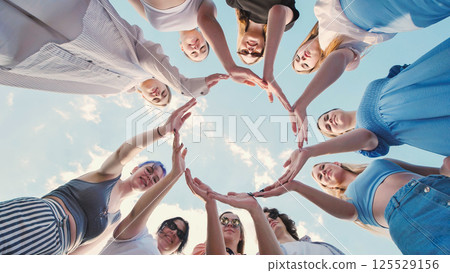 Group of school friends forming a circle with their hands against a blue sky, demonstrating unity, teamwork, and collaboration 125529156
