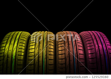 Studio shot of a set of summer car tires in yellow and pink tones. Tire stack background. Car tyre protector close up. Black rubber tire. Brand new car tires. Close up tyre profile. Car tires in a row Studio shot of a set of summer car tires in yellow and pink tones. Tire stack background. Car tyre protector close up. Black rubber tire. Brand new car tires. Close up tyre profile. Car tires in a row 125529160