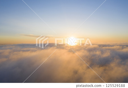 Aerial view gold sunrise over clouds in blue sky. Aerial top view cloudscape. Texture of clouds. View from above. Orange sunrise or sunset over clouds. Panorama clouds texture 125529188