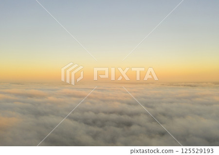 Aerial view gold sunrise over clouds in blue sky. Aerial top view cloudscape. Texture of clouds. View from above. Orange sunrise or sunset over clouds. Panorama clouds texture 125529193