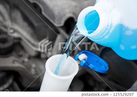 Pouring liquid from plastic canister into car washer fluid reservoir. Close up filling windscreen water tank with washing liquid. Pouring liquid from plastic canister into car washer fluid reservoir. Close up filling windscreen water tank with washing liquid. 125529207