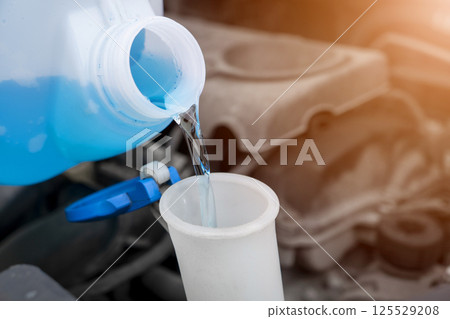 Pouring liquid from plastic canister into car washer fluid reservoir. Close up filling windscreen water tank with washing liquid. 125529208