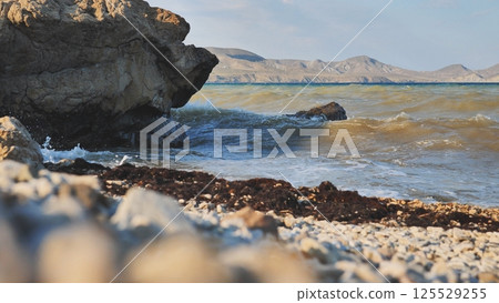 Waves crashing on Crimean rocky beach at sunset with mountains in background 125529255