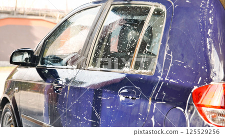 Car wash worker covering blue car with soap during cleaning service Car wash worker covering blue car with soap during cleaning service 125529256