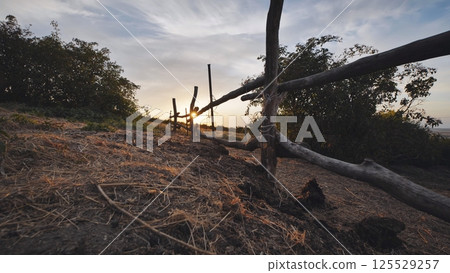 Weathered wooden fence separating farmland, casting long shadows during golden hour light Weathered wooden fence separating farmland, casting long shadows during golden hour light 125529257