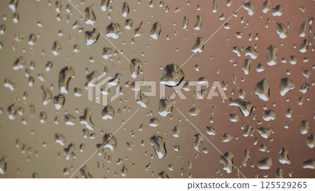 Raindrops sliding on a window during a rainy day reflecting a building 125529265
