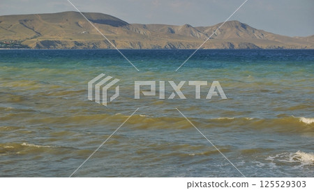 Gentle waves caressing sandy shoreline, tranquil black sea waters revealing distant crimean coastline under soft light 125529303