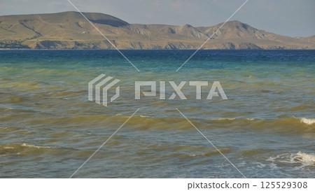 Gentle waves caressing sandy shoreline, tranquil black sea waters revealing distant crimean coastline under soft light Gentle waves caressing sandy shoreline, tranquil black sea waters revealing distant crimean coastline under soft light 125529308