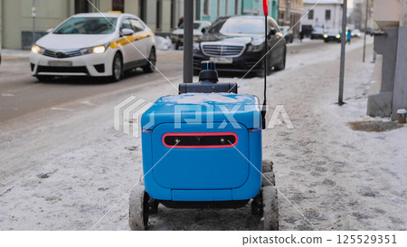 Autonomous delivery robot moving on a snowy sidewalk, navigating urban environment in Moscow. Autonomous delivery robot moving on a snowy sidewalk, navigating urban environment in Moscow. 125529351