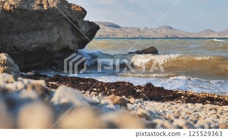 Waves crashing on Crimean rocky beach at sunset with mountains in background Waves crashing on Crimean rocky beach at sunset with mountains in background 125529363