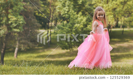 Young girl in pink dress strolling through sunny park with lush green landscape Young girl in pink dress strolling through sunny park with lush green landscape 125529369