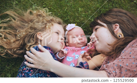 Mother, daughter, and baby lying together on lush grass, embracing each other and cherishing joyful family moments in nature Mother, daughter, and baby lying together on lush grass, embracing each other and cherishing joyful family moments in nature 125529500