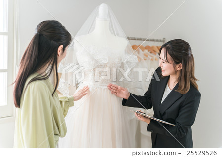 一位女士正在與婚禮策劃師和禮服協調員開會，選擇禮服 125529526