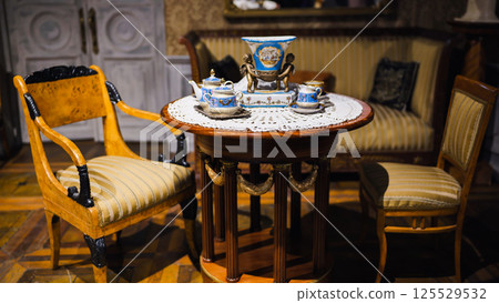 Antique tea set displayed on elegant wooden table with chairs in vintage room 125529532