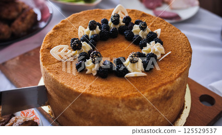 Cutting delicious sponge cake decorated with blackberries and white chocolate on festive table 125529537