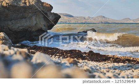 Powerful waves smashing rocky crimean coastline, rugged mountains looming across dark black sea waters, dramatic seascape unfolding 125529649