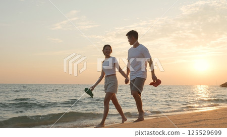 Vacation loving couple walking on beach together at sunset landscape, relaxing vacation travel summer, Asian man and woman in love holding hands walks along the sandy seashore Vacation loving couple walking on beach together at sunset landscape, relaxing vacation travel summer, Asian man and woman in love holding hands walks along the sandy seashore 125529699