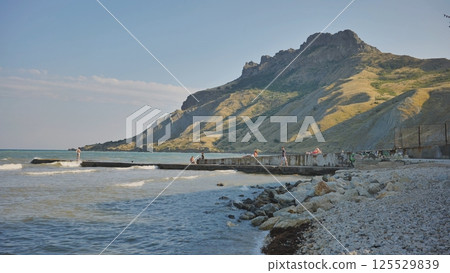 Tourists relaxing on Koktebel beach under Kara Dag mountain in Crimea Tourists relaxing on Koktebel beach under Kara Dag mountain in Crimea 125529839