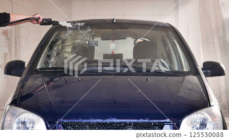 Car wash worker cleaning windshield with high pressure water jet 125530088