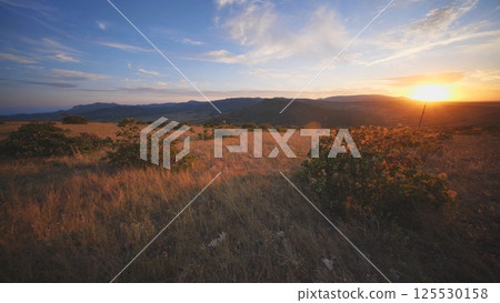 Crimean sunset illuminating dry meadow and distant mountains Crimean sunset illuminating dry meadow and distant mountains 125530158