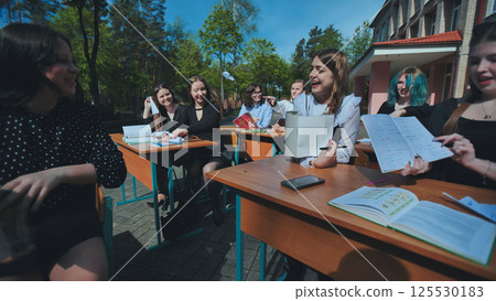 Cheerful teenagers studying and chatting together at outdoor desks on a sunny school day 125530183