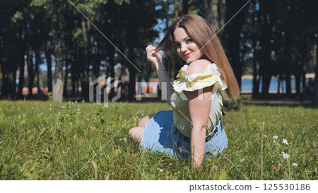 Teenager girl enjoying a sunny day in the park, playing with her hair and smiling joyfully while surrounded by nature's beauty 125530186