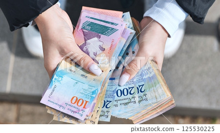Woman clutching worthless venezuelan bolivar bills, revealing hyperinflation's devastating economic impact Woman clutching worthless venezuelan bolivar bills, revealing hyperinflation's devastating economic impact 125530225