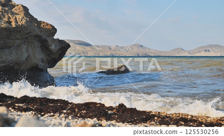 Foaming waves pounding rocky crimean shoreline with mountainous peninsula silhouette 125530256