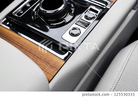 Modern luxury car white leather interior with natural wood panel. Part of leather car seat details with stitching. Interior of prestige modern car. White perforated leather. Car detailing. Car inside 125530333