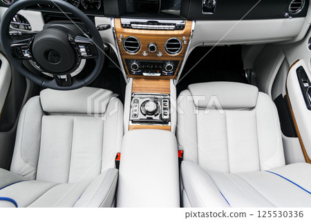 Modern luxury car white leather interior with natural wood panel. Part of leather car seat details with stitching. Interior of prestige modern car. White perforated leather. Car detailing. Car inside 125530336