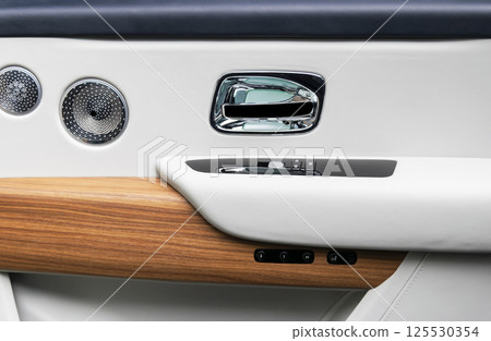 Door handle with power window control buttons of a luxury passenger car. White perforated leather interior with stitching and natural wood panel. Modern car interior details. Car detailing. Car inside 125530354