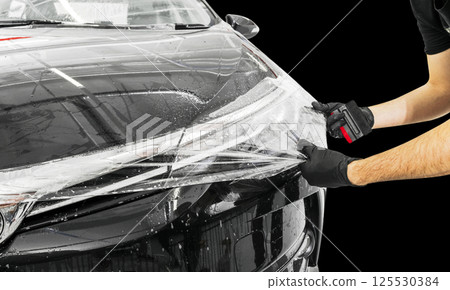 Car wrapping specialist putting vinyl foil or film on car. Protective film on the car. Applying a protective film to the car with tools. Car detailing. Transparent film. Car paint protection. isolated Car wrapping specialist putting vinyl foil or film on car. Protective film on the car. Applying a protective film to the car with tools. Car detailing. Transparent film. Car paint protection. isolated 125530384