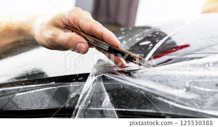 Car wrapping specialist cutting vinyl foil or film on car. Protective film. Applying a protective film with tools for work. Car detailing. Transparent film. Car paint protection. Trimming. 125530388