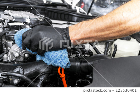 A man cleaning car engine with microfiber cloth. Car detailing or valeting concept. Selective focus. Car detailing. Cleaning with sponge. Worker cleaning. Car wash concept solution to clean A man cleaning car engine with microfiber cloth. Car detailing or valeting concept. Selective focus. Car detailing. Cleaning with sponge. Worker cleaning. Car wash concept solution to clean 125530401