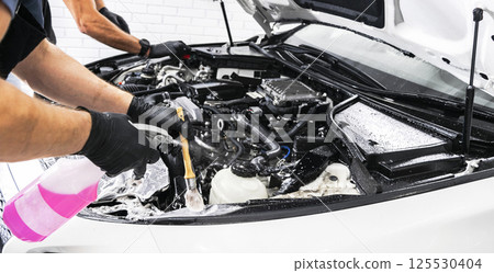 A man cleaning car engine with shampoo and brush. Car detailing or valeting concept. Selective focus. Car detailing. Cleaning with sponge. Worker cleaning. Car wash concept solution to clean A man cleaning car engine with shampoo and brush. Car detailing or valeting concept. Selective focus. Car detailing. Cleaning with sponge. Worker cleaning. Car wash concept solution to clean 125530404