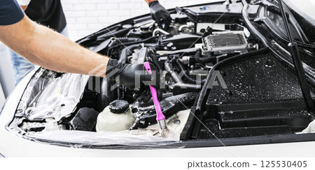 A man cleaning car engine with shampoo and brush. Car detailing or valeting concept. Selective focus. Car detailing. Cleaning with sponge. Worker cleaning. Car wash concept solution to clean 125530405