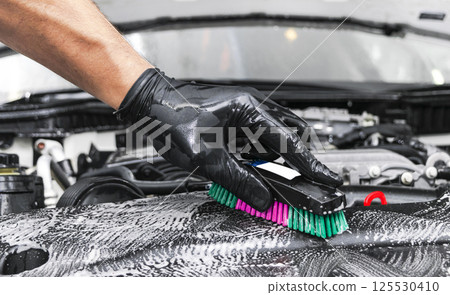 A man cleaning car engine with shampoo and brush. Car detailing or valeting concept. Selective focus. Car detailing. Cleaning with sponge. Worker cleaning. Car wash concept solution to clean A man cleaning car engine with shampoo and brush. Car detailing or valeting concept. Selective focus. Car detailing. Cleaning with sponge. Worker cleaning. Car wash concept solution to clean 125530410