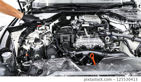 A man cleaning car engine with shampoo and brush. Car detailing or valeting concept. Selective focus. Car detailing. Cleaning with sponge. Worker cleaning. Car wash concept solution to clean 125530413