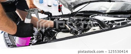 A man cleaning car engine with shampoo and brush. Car detailing or valeting concept. Selective focus. Car detailing. Cleaning with sponge. Worker cleaning. Car wash concept solution to clean 125530414