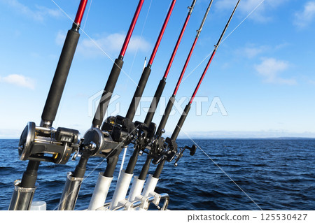 Fishing trolling boat rods in rod holder. Big game fishing. Fishing reels and rods pattern on boat. Sea fishing rods and reels in a row 125530427