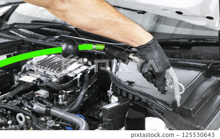 Car detailing maintenance. Cleaning engine with hot steam. High pressure washing. Washing at the station. Car washing concept. Car detailing. A man cleaning car. Cleaning engine with the foam and a 125530643